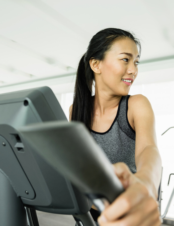 Asian woman exercising on Elliptical trainer machine at the gym.