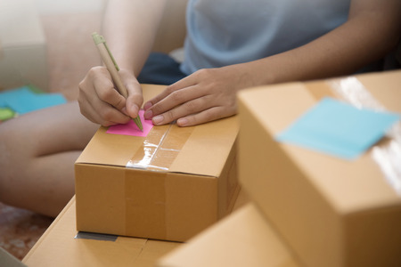 Close up Asian woman checking supplies and writing on cardboard box in her small warehouse. Own businessの写真素材