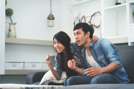 Cheerful beautiful young Asian couple watching TV at home.の写真素材