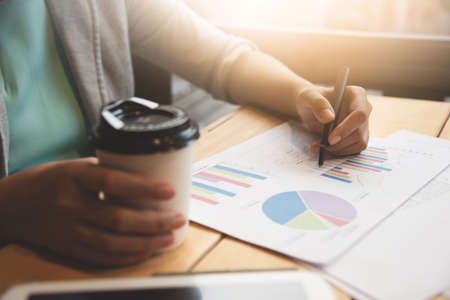 Close up of business woman hands writing on documents and holding cup of coffee.