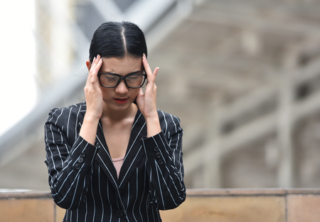 Stressed Asian Business woman having headache from overtime working at outdoor. Copy space.の写真素材