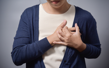 Young Asian glasses woman having chest pain from heart attack and standing on gray background. Copy space. Illness, exhausted, disease, tired for overtime working concept.の写真素材