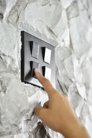 Close up hand turning on or off on grey or black lighting switch on rough stone wall. Copy space.の写真素材