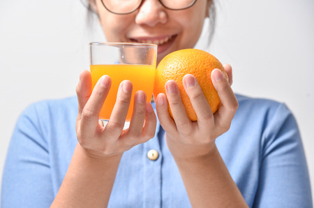 Beautiful Young Asian Woman in blue shirt smiling and holding orange with Orange juice in hands on white background. Diet healthy food.の写真素材