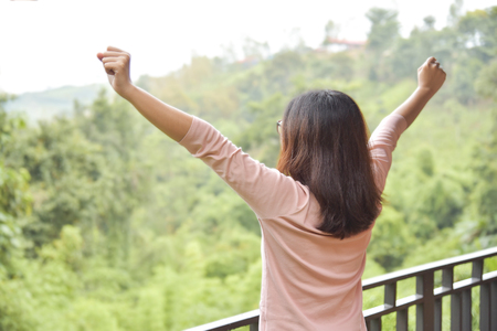 Rear view. Happy, Relaxed Asian woman waking up and Outstretched her arms on green natural background at balcony in the morning. Resting on Holiday.の写真素材