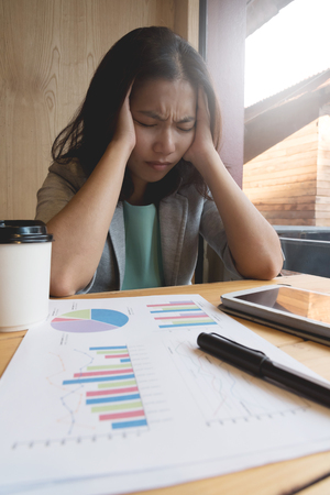 Stressed of Asian Business woman having headache from overtime working with tablet, pen documents and cup of coffee at the office.の写真素材
