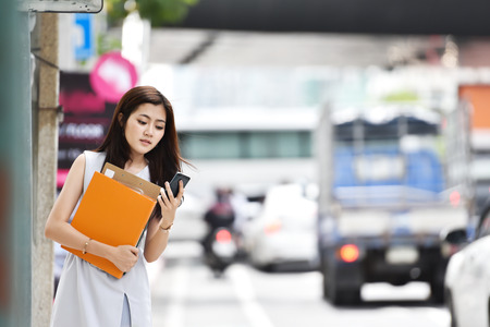 Asian Business woman using mobile phone while waiting for a cab in a city.  copy space.の写真素材