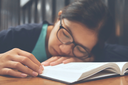Tired Asian woman sleeping with her book on wooden table.の写真素材