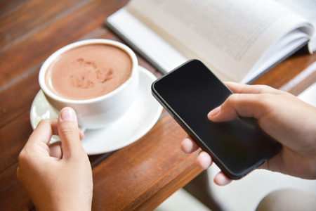 Close up Asian Woman Hands using smart phone and holding a cup of coffee.の写真素材