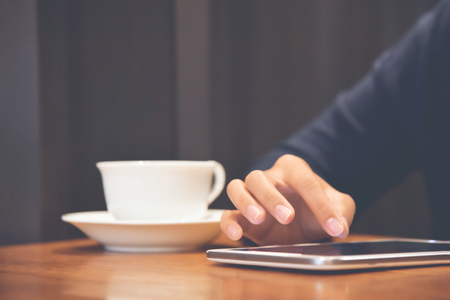 Close up woman hand using tablet computer with white cup of coffee on wooden table at coffee shop.の写真素材