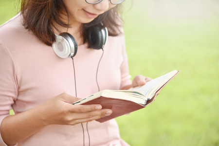 Happy Beautiful Asian Woman in Glasses with headphone reading book or diary at natural outdoor park. copy space.の写真素材