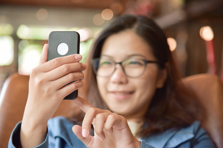 Happy Beautiful Asian Woman in blue shirt smiling and taking seifies photo with her smart phone at coffee shop.の写真素材