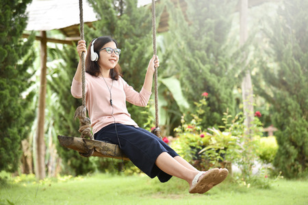 Happy Asian Young beautiful woman in Glasses listening music and holding rope of swing at Park outdoor. Smiling face. Copy space.の写真素材