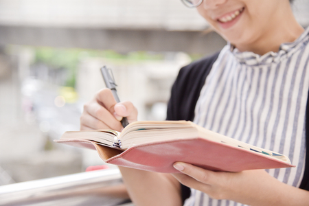 Happy Asian Business Woman writing on notebook in the city. Appointment, negotiation and reminder for business concepts. Copy space.の写真素材