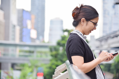 Relaxed Chinese Business Woman using smart phone on skyscraper building background in the city. Copy space.の写真素材