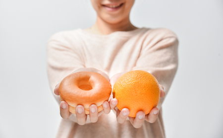 Dieting concept. Beautiful Young Asian Woman holding orange and chocolate donut on white background.
Choosing between junk food with healthy food.の写真素材