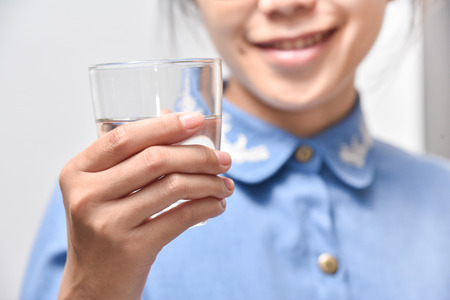 Healthy Lifestyle. Happy Asian woman in blue shirt holding glass of water on white background.
