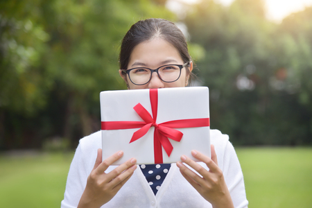 Asian female holding a white gift box on green nature background for Birthday, Christmas and New year.の写真素材