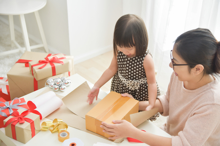 Young mother and her daughter wrapping a gift box for Birthday, Christmas and New year in a white room. Happy Asian family at the house. Copy space.の写真素材