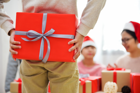 Making a surprise for Christmas and New year. Asian Boy are hiding red gift box behind his back while his family are sitting.の写真素材