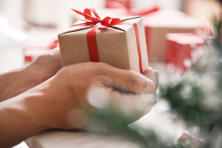 Male hands holding a brown present box with red ribbon on white marble background for Christmas and New year. Top view.の写真素材
