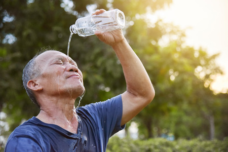 Asian senior male pouring water from bottle on his face after exercise at park outdoor background. Washing. Cleaning.の写真素材