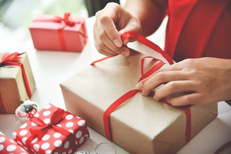 Female hands wrapping  present boxes white table for Christmas and New year.