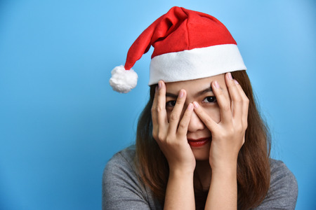 Portrait of Asian female wear Glasses and Santa Claus hat smiling and holding her face with her hands on Blue background. Christmas and New year concept. Happy. Fashion.の写真素材