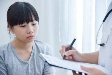 Asian Female Doctor taking note on checklist paper for a little girl patients.の写真素材