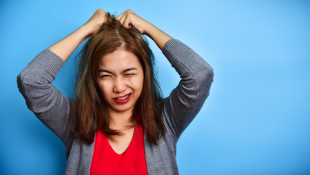 Portrait of a stressed Asian woman in red shirt holding head in hands on blue background.の写真素材