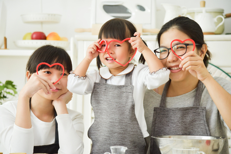 Happy Asian family holding red hearts shape while baking cookies and cakes in the kitchen together.の写真素材