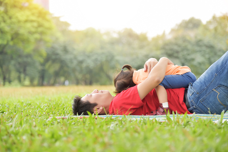Happy young Asian father and his daughter are hugging together and sleeping on the grass in nature at park outdoor. Family.の写真素材