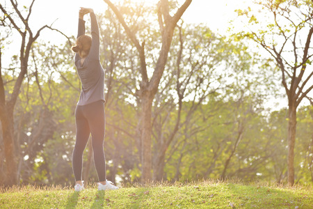 Happy Asian female in grey sportswear workout at the park. Young woman is standing and warming up...
