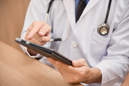 Close up Asian male Doctor hands using and pointing on digital tablet computer on wooden desk. Medical and health care concept.の写真素材