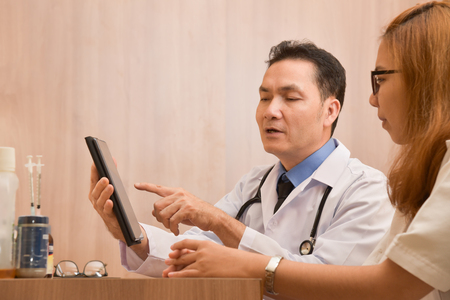 Close up Asian senior male Doctor using digital tablet computer and discussing with female doctor. Medical and health care concept.の写真素材