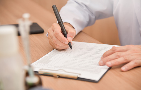Close up on hands. Asian male doctor is writing something on clipboard, prescription, paper work,patient check list paper or application form.の写真素材