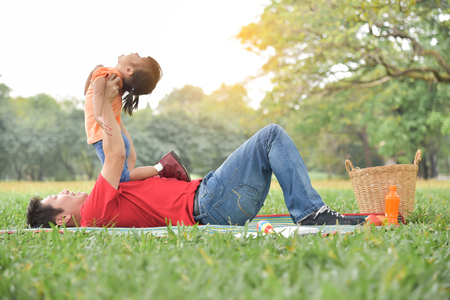 Happy young Asian father and his daughter lying on the grass and playing together in nature at park outdoor. Family Having fun.の写真素材
