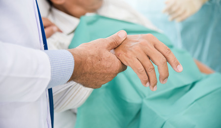 Close up on hands. Male doctor is checking a senior man patient pulse in a medical room. Health...