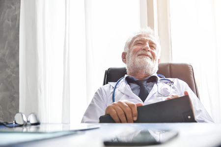 Happy Senior male Doctor is thinking and smiling in a Medical room. Successful.の写真素材