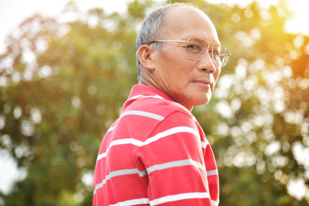 Portrait of Confident Asian Senior male wear glasses in red shirt smiling on green natural...