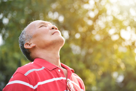 Portrait of Asian Senior male in red shirt breathing fresh air on green natural background at park outdoor.の写真素材