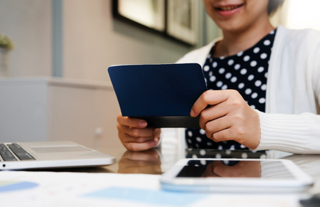 Beautiful Asian female smiling. Happy Young Business woman holding saving account passbook. Successful. Laptop, tablet on desk at working room.の写真素材