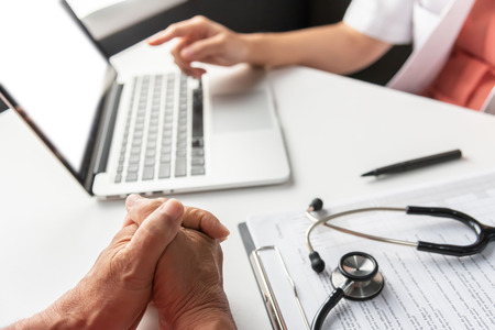 Selective Focus on male hands. Female Doctor discussing with senior man patient on laptop in medical...