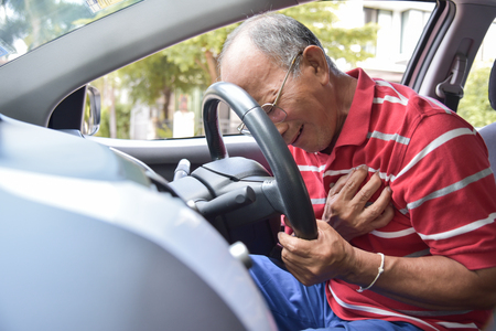 Asian Senior man in red shirt having chest pain from heart attack while driving a car.  Illness, exhausted, disease.の写真素材