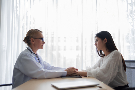 Senior Female doctor talking and reassuring Young Asian woman patient with holding hands in medical room.の写真素材
