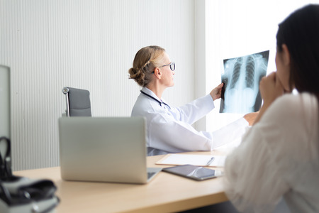 Senior Female doctor examining and looking to X-ray film of her patient at a medical room.の写真素材
