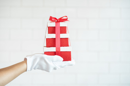 Close up Girl hands wear white gloves holding red gift boxes over white brick wall with copy space....