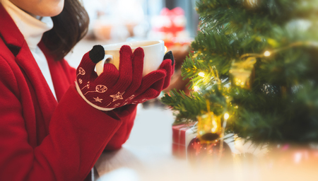 Asian woman in red sweater clothes and gloves holding a cup of coffee in winter day. Copy space. Christmas.の写真素材