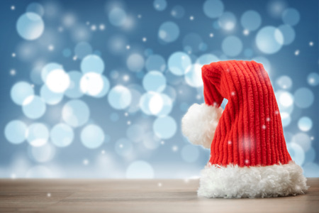 Red Santa Claus hat with copy space over Blurred bokeh of Christmas lights, snow and snowflakes background.の写真素材