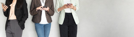 Cropped image of Group of Young Businesswomen using smartphones while standing over grey bare wall....